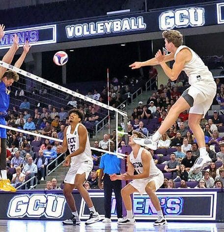 rise above the block in America A Grand Canyon University (GCU) men's volleyball player smashes the ball over a three-man block in a packed arena during an NCAA Division 1 match.