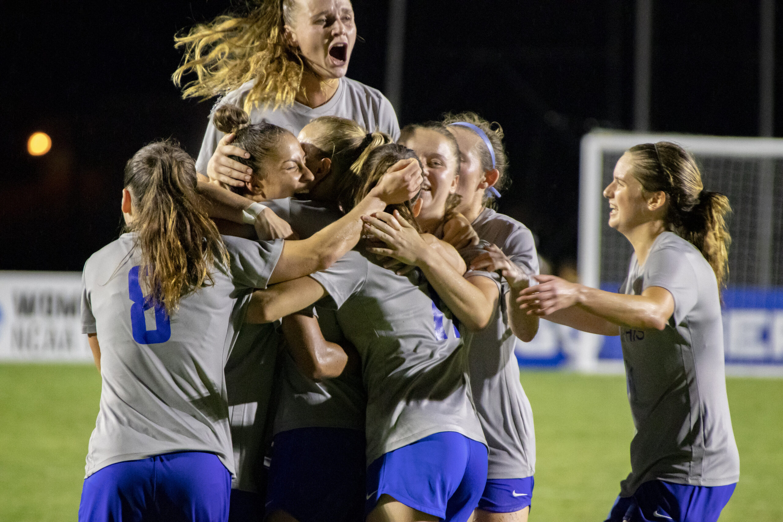 kimberley-smit-memphis-soccer-team-celebration Het damesvoetbalteam van de University of Memphis, met de Nederlandse speelster Kimberley Smit, viert uitbundig een doelpunt in een groepsknuffel op het veld.