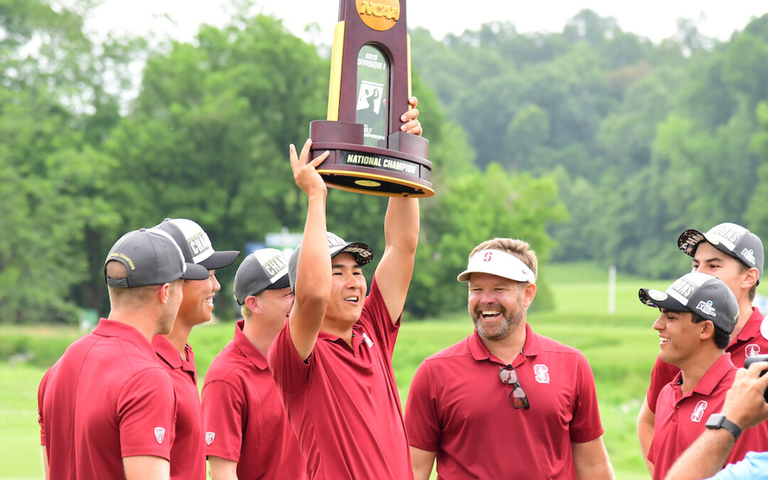 Een mannelijke college golfer tilt de NCAA National Championship trofee juichend omhoog, omringd door zijn lachende teamgenoten en coach.