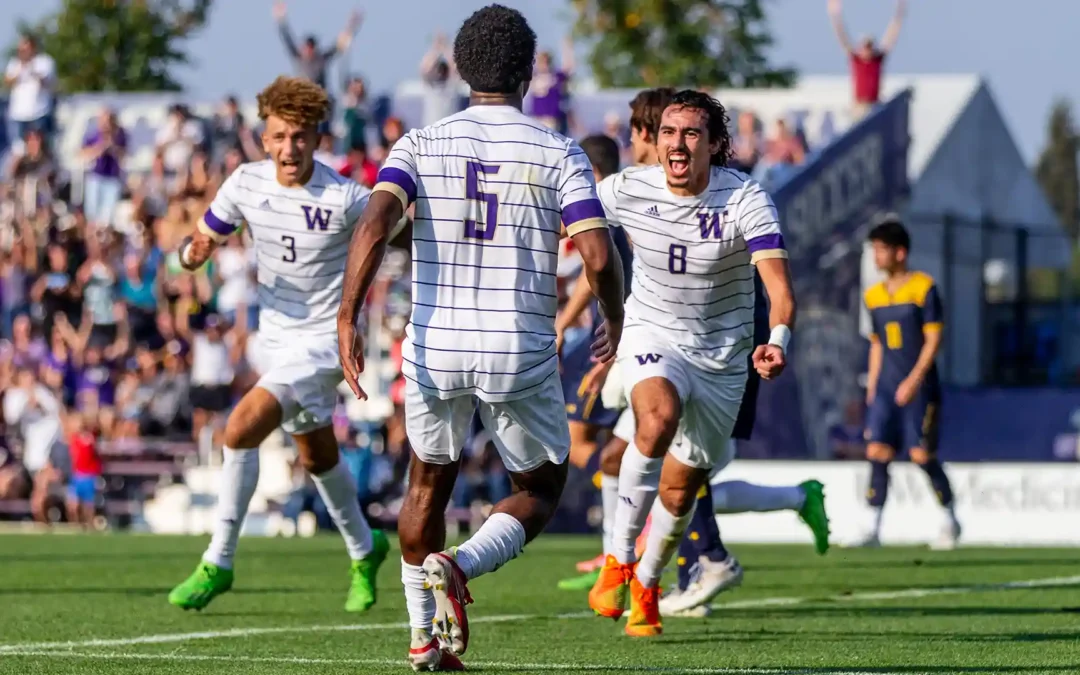 Drie spelers van het mannenvoetbalteam van de University of Washington (in wit-paarse strepen) juichen uitbundig na een doelpunt tijdens een NCAA college soccer wedstrijd.