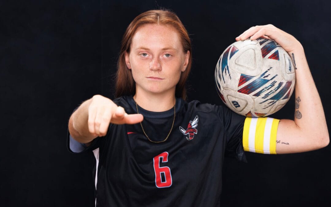 Megan Castricum, voetbalster bij Delaware State University, poseert in haar teamshirt met een bal op haar schouder