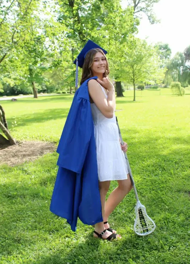 Afstuderen als student-athlete in Amerika | Lacrosse Scholarship Student-athlete poseert in afstudeerkleding met een lacrossestick na het behalen van haar diploma aan een Amerikaanse universiteit.