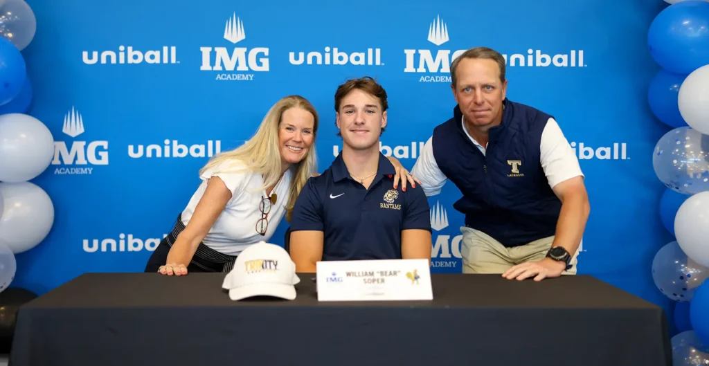 Een jonge mannelijke student-athlete in een poloshirt tekent een contract aan een tafel met zijn ouders, voor een achtergrond van de IMG Academy