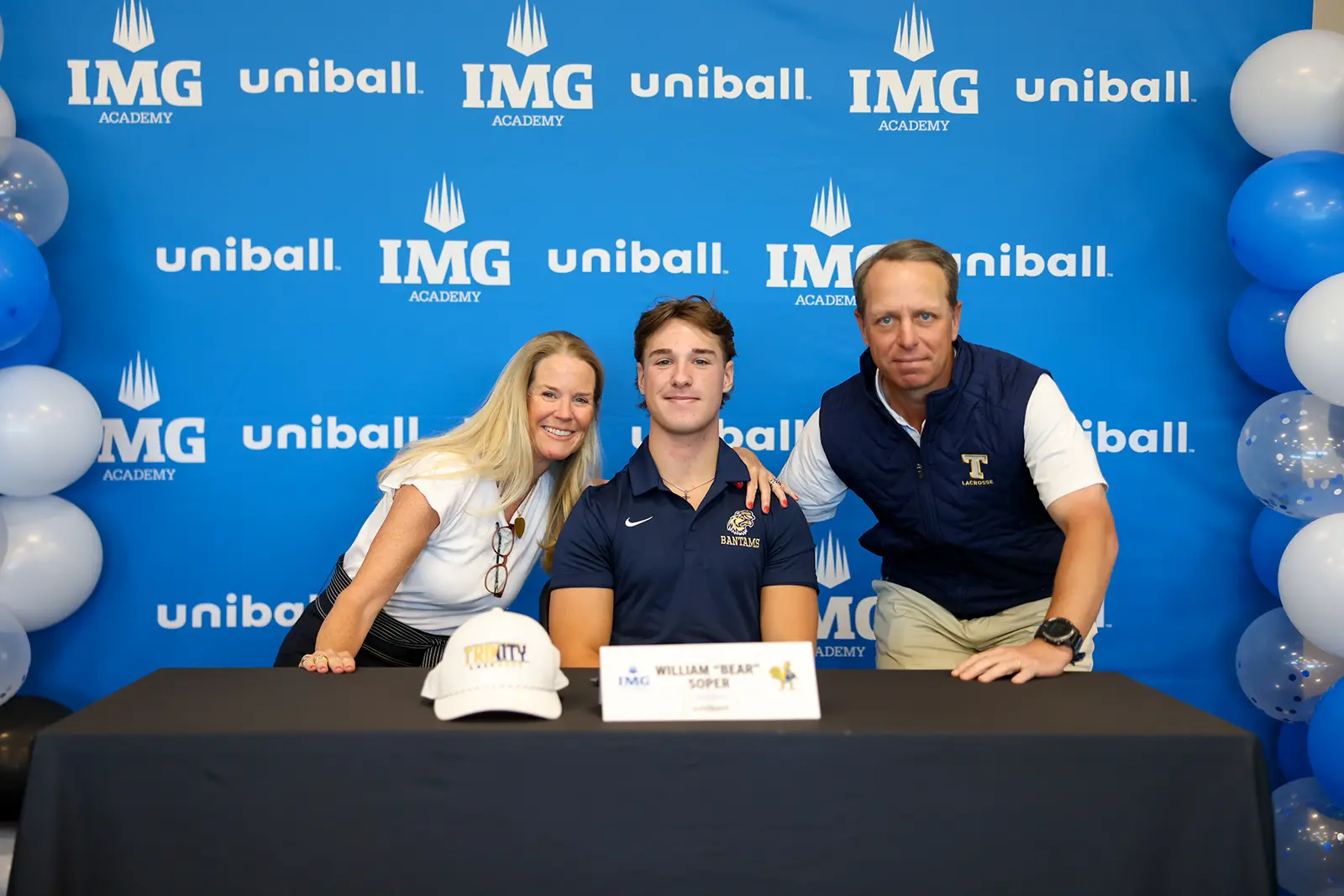 Een jonge mannelijke student-athlete in een poloshirt tekent een contract aan een tafel met zijn ouders, voor een achtergrond van de IMG Academy