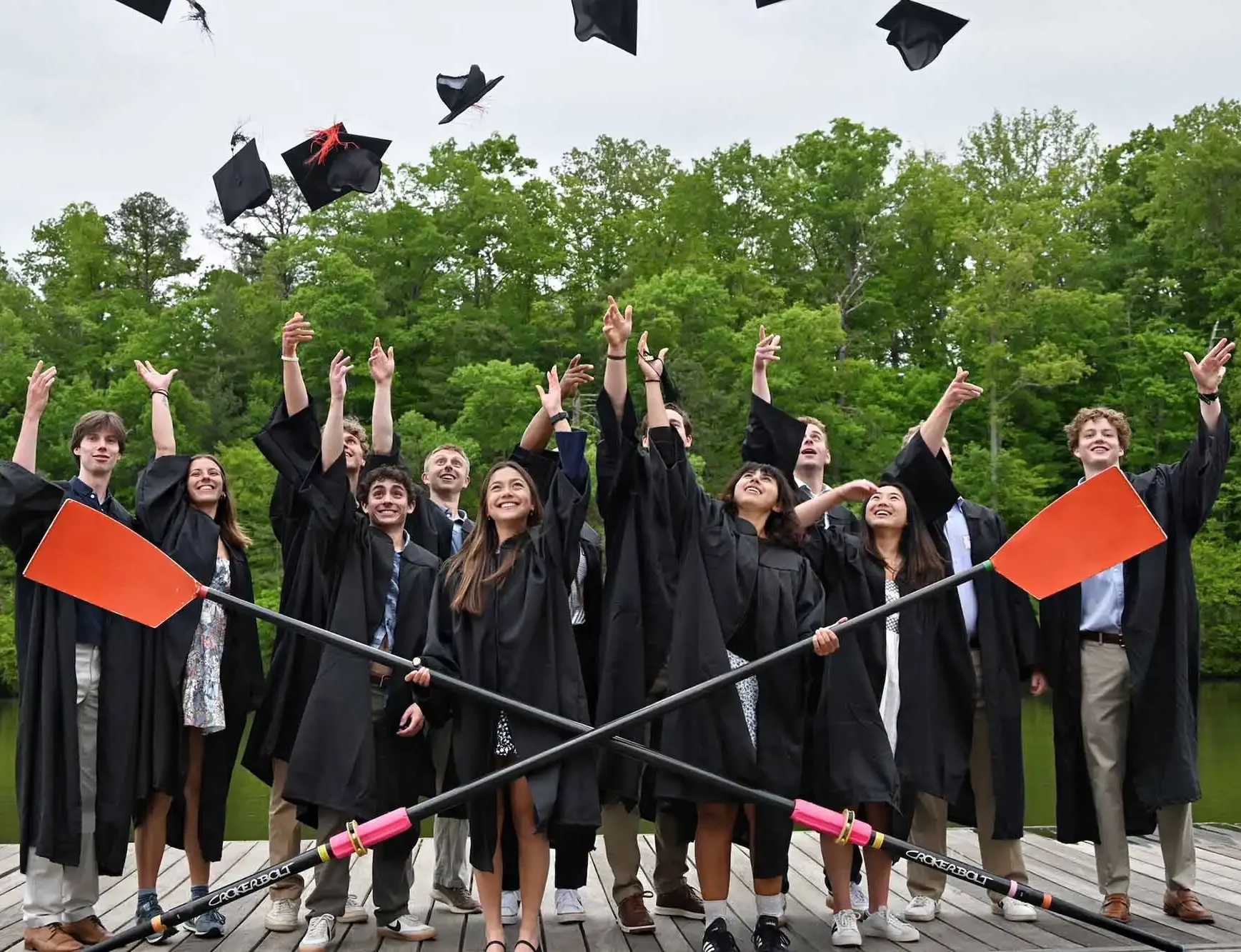 Roeien en studeren in Amerika Afgestudeerde student-athletes in toga gooien hun afstudeerhoeden omhoog naast roeiriemen.
