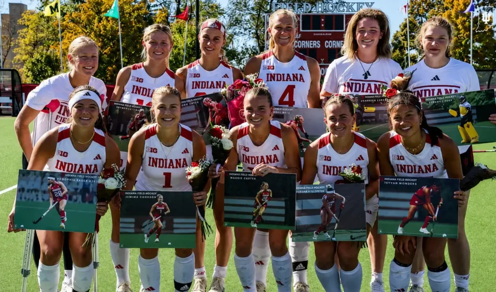 College field hockey players celebrating Senior Day on the field with flowers, framed action photos, and Indiana uniforms.