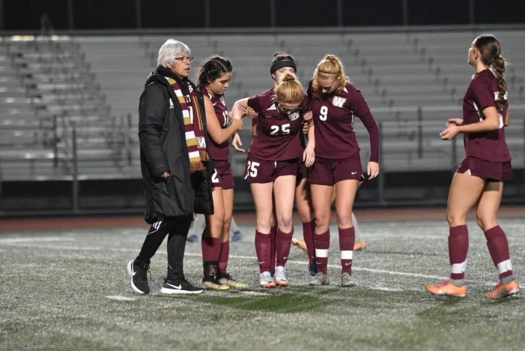 Geblesseerde student-athlete wordt van het veld geholpen door teamgenoten en coach